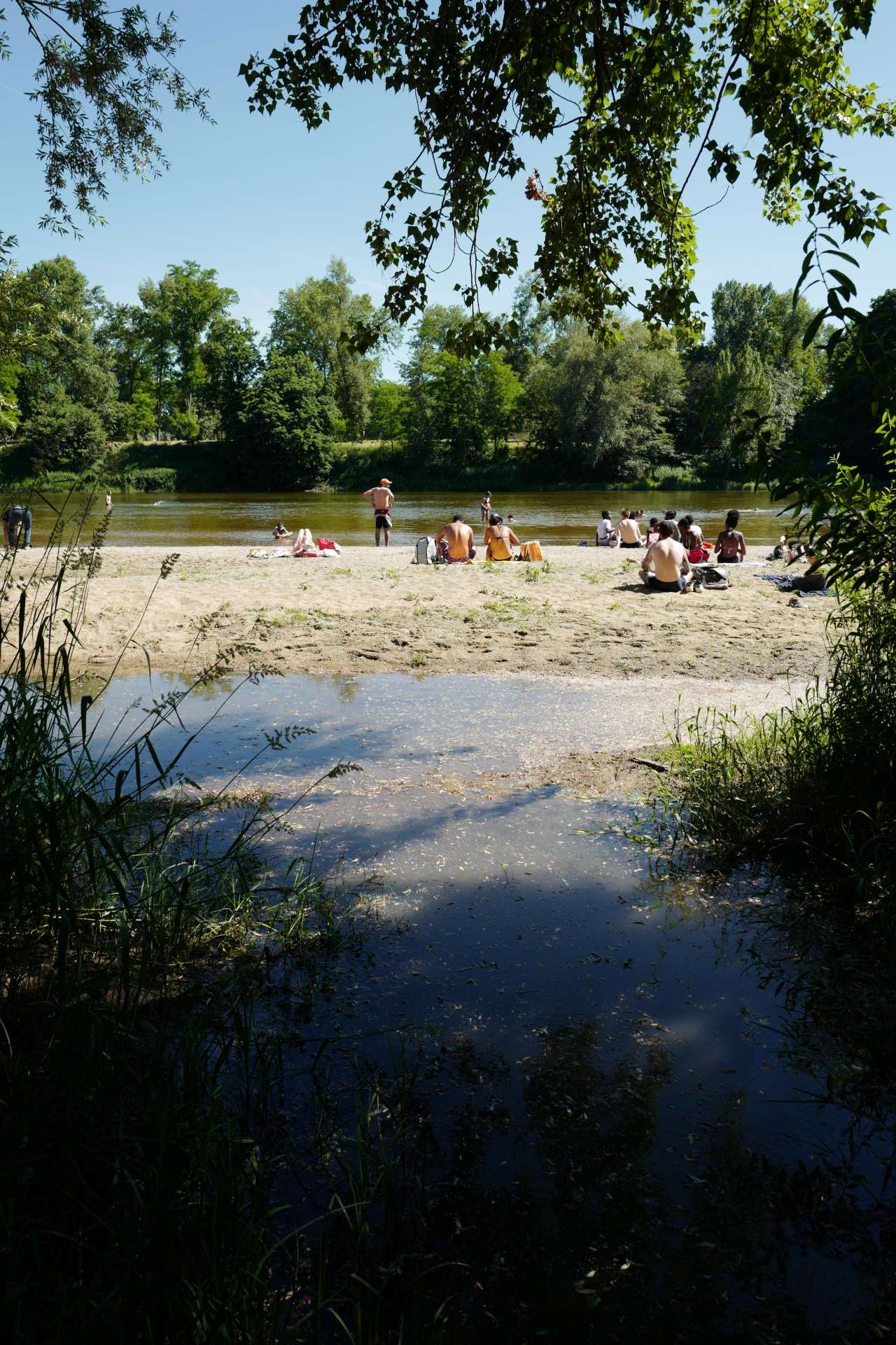 Photo de personnes en tenue de plage, assises sur un banc de sable en bord de Loire, l'été.